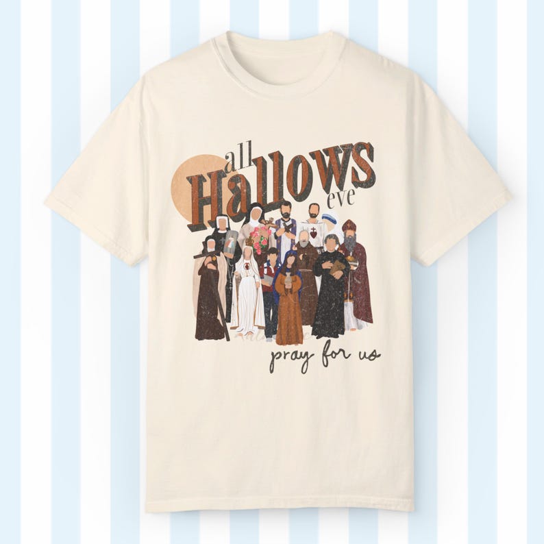 K&ouml;nnte beinhalten: Ein beiges T-Shirt mit einer Grafik im Vintage-Stil einer Gruppe von Personen in religi&ouml;ser Kleidung. Die Grafik lautet "all Hallows eve pray for us".