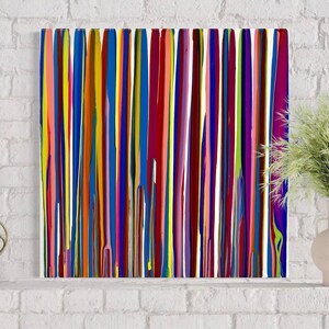 Op de afbeelding: Abstract kunstwerk met verticale strepen in levendige kleuren, waaronder rood, blauw, geel en groen. Het kunstwerk heeft een glanzende afwerking en wordt getoond op een witte bakstenen muur. Een moderne, kleurrijke toevoeging aan elk interieur.