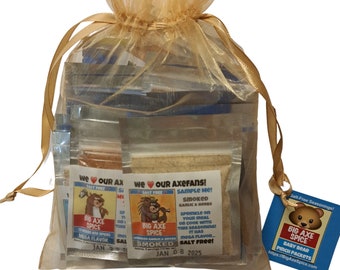 Puede incluir: Una bolsa de organza dorada llena de pequeños paquetes de mezcla de condimentos Big Axe Spice. Los paquetes presentan un logotipo de oso de dibujos animados y el texto "We love our Axefans! Sample Me! Smoked Garlic & Herbs". Una etiqueta separada con un logotipo de oso de dibujos animados dice "Salt-Free Seasonings! Big Axe Spice Baby Bear Pinch Packets https://BigAxeSpice.com"