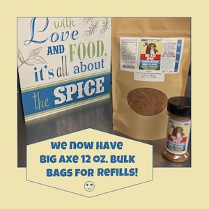 May include: A brown paper bag filled with a red spice blend. The bag has a label that says "Big Axe Spice Mega Flavor" and "Bulk 12 oz. (340 g)". A smaller container of the same spice blend is also shown. The text "We now have Big Axe 12 oz. Bulk Bags for Refills!" is displayed below the image.