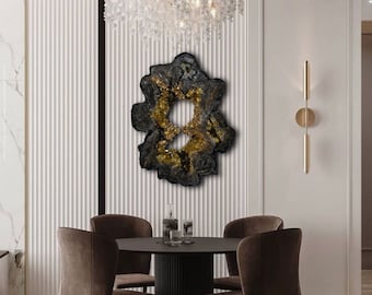 Op de afbeelding: Een moderne eetkamer met een zwarte ronde tafel en vier bruine stoelen. Boven de tafel hangt een groot, abstract zwart en goudkleurig kunstwerk. Een decoratieve kroonluchter met hangende kristallen is zichtbaar. De muren zijn wit met verticale panelen.