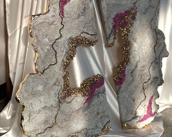 Könnte beinhalten: Zwei abstrakte Wandkunststücke mit weißem, grauem und goldenem Hintergrund. Die Stücke haben eine einzigartige, organische Form mit einem pinkfarbenen und goldenen Glitzerdesign.