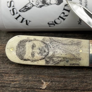 May include: A pocket knife with a portrait on the handle, and two open blades. The handle has a portrait of a person and the words "BOWDE" below it. The knife is next to a white cylinder with the words "MISSOURI SCRIMSHAW" and a donkey illustration.