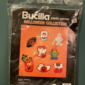May include: A Bucilla plastic canvas Halloween collection kit in a clear plastic bag. The kit includes eight "Spooky" ornaments with various Halloween-themed designs, such as ghosts, pumpkins, and monsters. The kit is designed by Bonnie Smith.