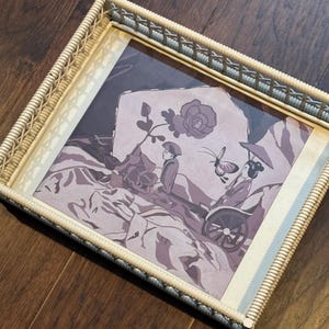 May include: A wicker tray with a framed print of a Japanese scene. The print features two figures in traditional clothing, a butterfly, and a flower. The colors are muted and the overall tone is serene.