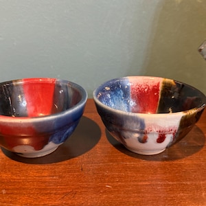May include: Two small ceramic bowls with a red, blue, and black glaze. The bowls are hand-painted and have a unique, rustic look.