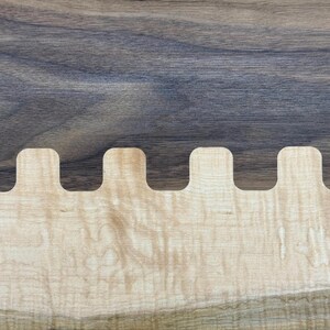 Op de afbeelding: Close-up van een houten oppervlak met een zwaluwstaartverbinding. Het bovenste gedeelte is donker, getextureerd hout, terwijl de onderkant lichter, patroonhout heeft. De verbinding is een reeks in elkaar grijpende rechthoekige vormen.