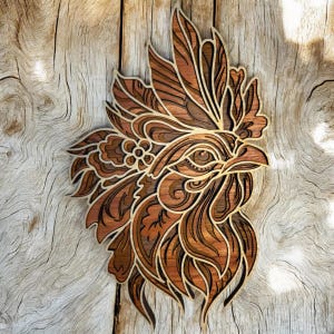 May include: Intricately carved wooden rooster head with a detailed design. The rooster's head is facing right and has a large comb and wattle. The wood is a rich brown color with a natural grain.