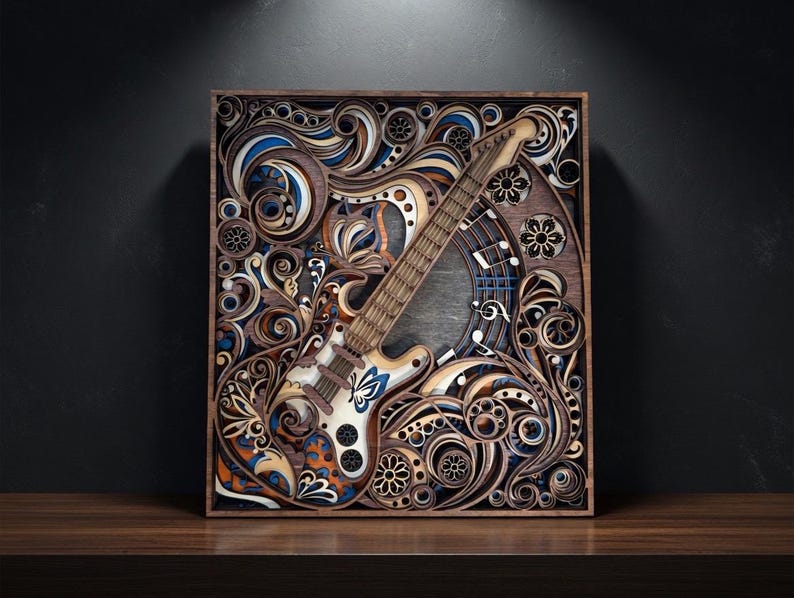 May include: A wooden, layered art piece featuring a guitar design. The guitar is white and brown, with blue and orange accents. The artwork is set within a dark brown frame, showcasing intricate floral and swirl patterns.