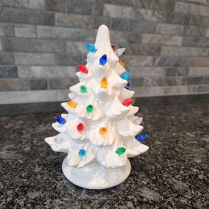 May include: A white ceramic Christmas tree with colorful lights. The tree is decorated with red, green, blue, yellow, and orange lights.