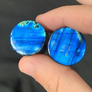 May include: Pair of blue and green labradorite stone ear gauges. The gauges have a smooth, polished finish and a unique, iridescent pattern.