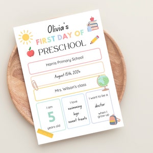 以下が含まれることがあります： カラフルなデザインの、幼稚園の初日用印刷可能なサイン。サインには、子供の名前、オリビア、学校の名称、ハリス・プライマリー・スクール、日付、2024年8月15日、教師の名前、ウィルソン先生、子供の情報、年齢5歳、好きな活動、水泳、レゴ、甘いお菓子、将来の職業への希望、医者になることが記載されています。
