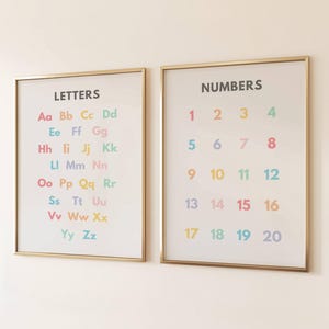 Könnte beinhalten: Zwei gerahmte Lernposter. Eines zeigt das Alphabet mit Groß- und Kleinbuchstaben in verschiedenen Farben. Das andere Poster zeigt die Zahlen 1-20. Beide Poster haben goldene Rahmen und sind an einer weißen Wand.