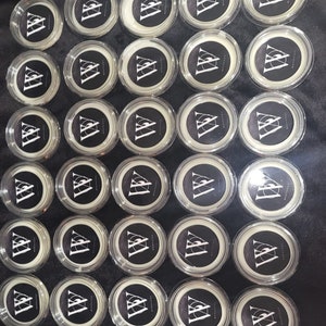 Könnte beinhalten: Eine Sammlung von 36 runden, transparenten Plastikbehältern mit weißen Deckeln. Jeder Behälter hat einen schwarz-weißen Aufkleber mit einem Dreiecksmuster und dem Text "Apothecary".