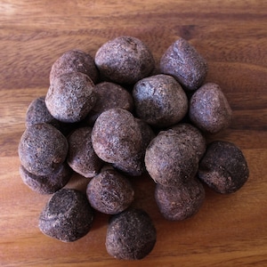 May include: A collection of dark brown truffles with an uneven, textured surface, arranged on a wooden background. The truffles are of varying sizes. The wood has a warm, natural grain.