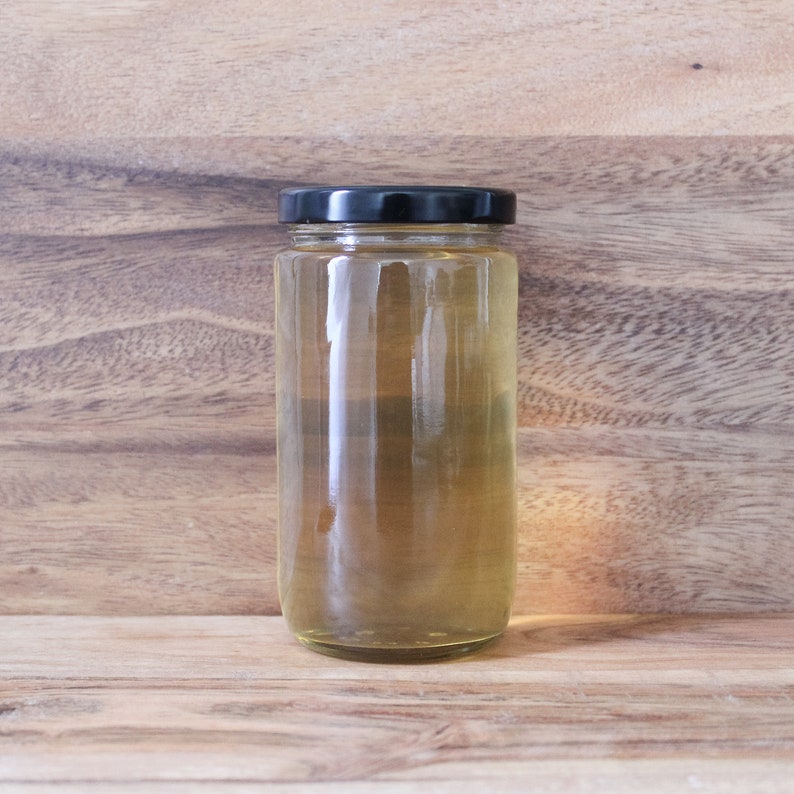 May include: A clear glass jar with a black lid filled with a light yellow liquid. The jar is sitting on a wooden surface.