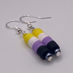 May include: A pair of silver dangle earrings with a yellow, white, purple, and black beaded design. The beads are stacked to resemble a flag.