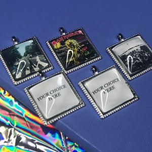 May include: Five silver-framed square pendants with different images. The images include a band, a crosswalk, and a crowd. Two pendants have the text "Your Choice Here".