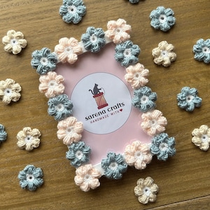 May include: A pink and blue crocheted flower frame with the text "sarena crafts handmade with" in the center. The frame is surrounded by smaller crocheted flowers in various colors.