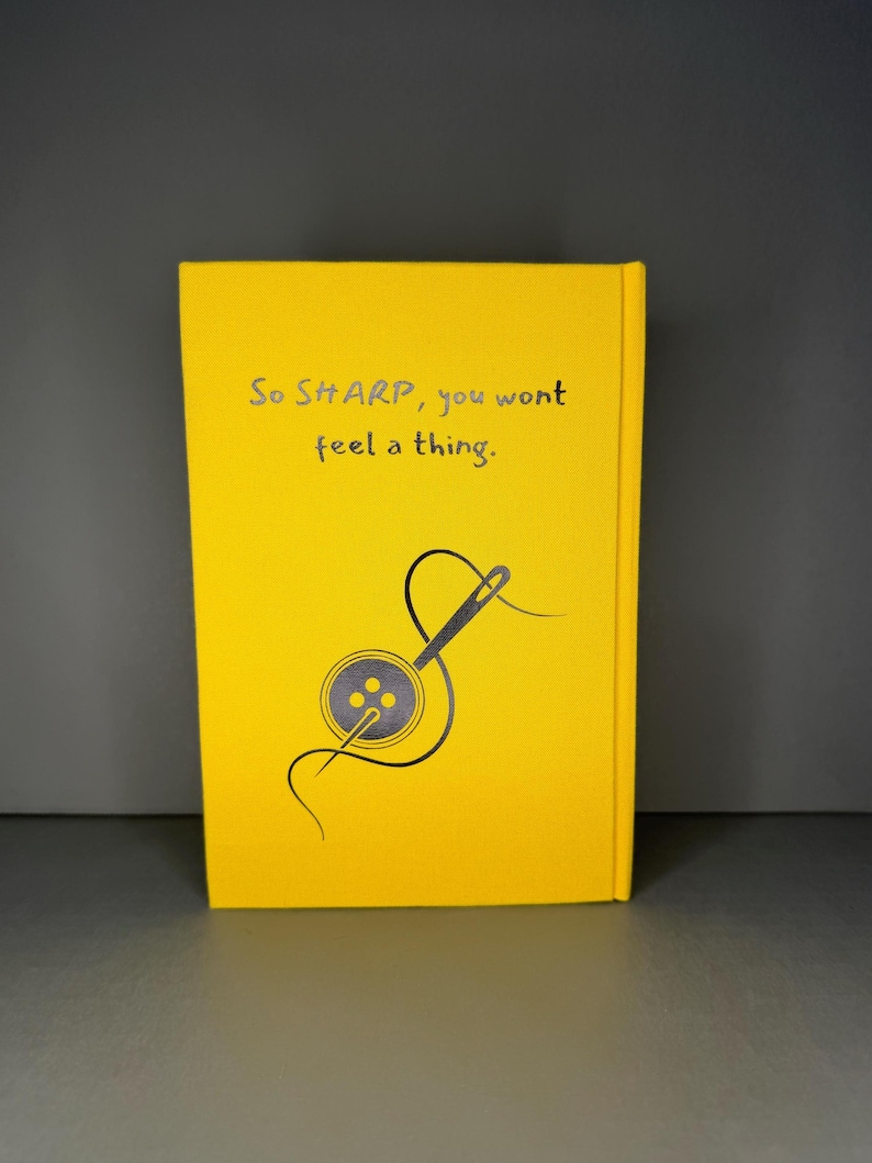 Puede incluir: Una cubierta de libro de color amarillo brillante con un gr&aacute;fico gris oscuro de una aguja de coser enhebrada a trav&eacute;s de un bot&oacute;n de cuatro agujeros. El texto impreso en gris oscuro dice: "So SHARP, you wont feel a thing." Fondo amarillo s&oacute;lido.
