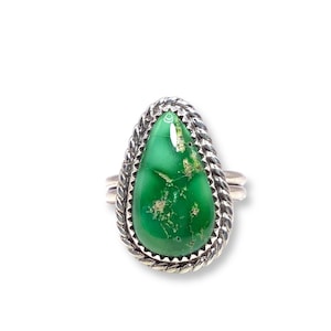 May include: A silver ring featuring a pear-shaped, vibrant green stone with a textured surface. The stone is set within a twisted rope-like border. The ring has a double band design.