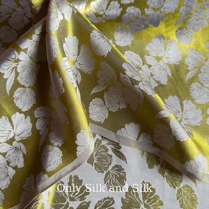 Könnte beinhalten: Nahaufnahme eines gefalteten Stoffes mit floralem Muster. Der Stoff hat eine leuchtend gelb-grüne Farbe mit weißen floralen Designs. Der Text "Only Silk and Silk" ist unten im Bild zu sehen.