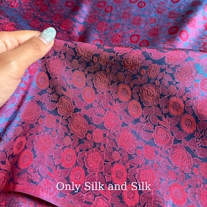 May include: Close-up of a silk fabric with a floral pattern. The fabric features a repeating design of red roses against a dark blue background. The text "Only Silk and Silk" is visible at the bottom of the image.