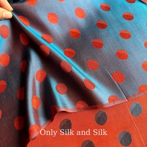 May include: A close-up of silk fabric with a teal and dark blue sheen. The fabric features a pattern of large, evenly spaced red polka dots. The text "Only Silk and Silk" is visible on the fabric.