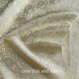 Könnte beinhalten: Nahaufnahme eines cremefarbenen Seidenstoffs mit floralem Muster. Der Stoff ist drapiert und zeigt Falten und Schatten. Der Text "Only Silk and Silk" ist unten im Bild zu sehen.