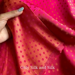 Könnte beinhalten: Nahaufnahme eines leuchtend rosa Seidenstoffs mit einem Polka-Dot-Muster. Der Stoff ist gefaltet und zeigt eine kontrastierende, orangefarbene Unterseite. Der Text "Only Silk and Silk" ist sichtbar.