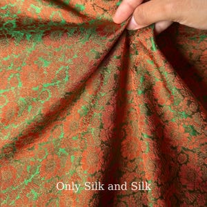 Könnte beinhalten: Nahaufnahme eines Stoffes mit floralem Muster in Orange- und Grüntönen. Der Stoff wird gehalten, wodurch seine Textur und sein Design sichtbar werden. Der Text "Only Silk and Silk" ist unten im Bild zu sehen.