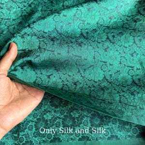 May include: Dark green silk fabric with a floral design. The fabric is folded, showing the texture and lustre of the material. The text "Only Silk and Silk" is visible at the bottom of the image.