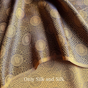 Könnte beinhalten: Nahaufnahme eines Seidenstoffs mit einem sich wiederholenden Muster aus goldfarbenen kreisförmigen Medaillons und geometrischen Formen auf dunklem braunem Hintergrund. Der Stoff ist gefaltet und zeigt die Unterseite mit dem Text "Only Silk and Silk".