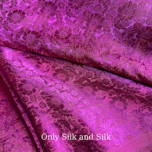 Könnte beinhalten: Nahaufnahme eines leuchtend pinkfarbenen Seidenstoffs mit floralem Muster. Der Stoff ist gefaltet, wodurch die Textur und der Glanz des Materials sichtbar werden. Der Text "Only Silk and Silk" ist unten im Bild zu sehen.