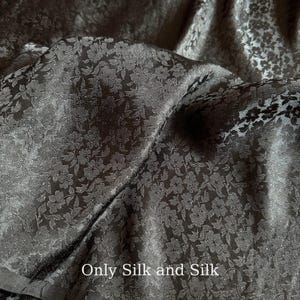 Könnte beinhalten: Nahaufnahme eines schwarzen Stoffes mit floralem Muster. Der Stoff ist gefaltet und zeigt seine Textur und seinen Glanz. Der Text "Only Silk and Silk" ist unten im Bild zu sehen.