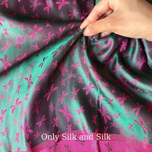 Può includere: Primo piano di un tessuto di seta con un motivo a libellule. Il tessuto ha un gradiente di colore da verde acqua a viola, con libellule rosa acceso. Il testo "Only Silk and Silk" è visibile in basso.