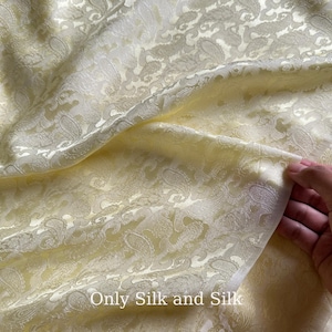 Könnte beinhalten: Nahaufnahme eines hellgelben Seidenstoffs mit Paisley-Muster. Der Stoff ist drapiert und zeigt Falten und Textur. Der Text "Only Silk and Silk" ist unten im Bild zu sehen.