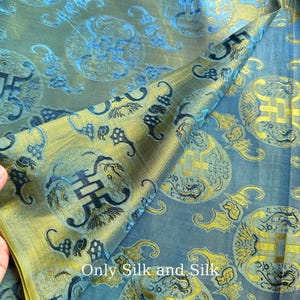 Peut inclure: Gros plan sur un tissu plié avec un effet chatoyant bicolore. Le tissu présente un motif répétitif de motifs circulaires et stylisés dans des tons de bleu et d'or. Le texte "Only Silk and Silk" est visible.