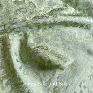 Könnte beinhalten: Nahaufnahme eines hellgrünen Seidenstoffs mit Paisley-Muster. Der Stoff hat einen subtilen Glanz und eine strukturierte Oberfläche. Der Text "Only Silk and Silk" ist unten sichtbar.