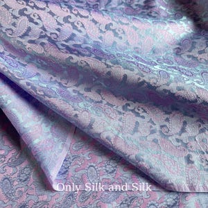 May include: Close-up of a luxurious fabric with a paisley pattern in shades of lavender, pink, and teal. The fabric is folded, showing the intricate design and texture. The text "Only Silk and Silk" is visible.