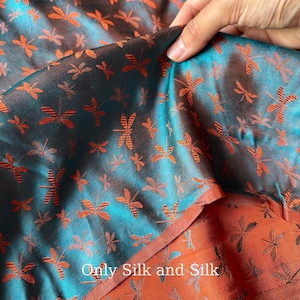 May include: A close-up of teal and rust-coloured silk fabric featuring a dragonfly pattern. The fabric is held up, showing the underside with the text "Only Silk and Silk". The dragonfly design is repeated across the material.