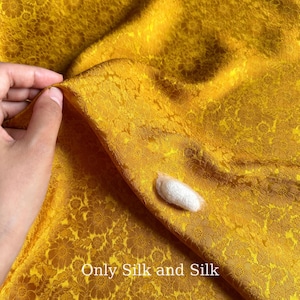 May include: Close-up of a golden yellow silk fabric with a floral pattern. A white silkworm cocoon rests on the fabric. The text "Only Silk and Silk" is visible at the bottom of the image.
