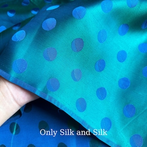 Könnte beinhalten: Nahaufnahme eines türkisblauen und blauen Seidenstoffs mit großen, gleichmäßig verteilten blauen Tupfen. Der Stoff ist gefaltet und gibt einen Blick auf die Unterseite frei. Der Text "Only Silk and Silk" ist in der unteren rechten Ecke zu sehen.