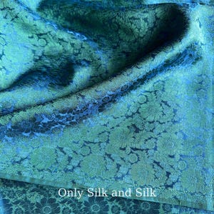 Könnte beinhalten: Nahaufnahme eines türkisfarbenen Seidenstoffs mit floralem Muster. Der Stoff ist drapiert und erzeugt Schatten und Glanzlichter. Der Text "Only Silk and Silk" ist unten im Bild zu sehen.