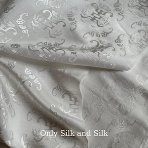 Peut inclure: Tissu de soie blanc avec un léger éclat, présentant un motif répété de symboles stylisés et de motifs floraux dans une nuance plus claire de blanc. Le texte "Only Silk and Silk" est visible en bas.