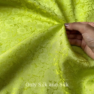 May include: Vibrant chartreuse silk fabric with a floral design. A hand holds up the fabric, highlighting its texture and flow. The text "Only Silk and Silk" is displayed at the bottom of the image.