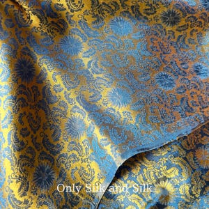 Könnte beinhalten: Nahaufnahme eines Stoffes mit floralem Muster in Gold- und Blautönen. Der Stoff hat eine strukturierte Oberfläche mit einem sich wiederholenden Design aus stilisierten Blumen und Paisley-Formen. Der Text "Only Silk and Silk" ist unten sichtbar.