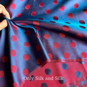Könnte beinhalten: Nahaufnahme eines Seidenstoffs mit blau-violettem Schimmer. Der Stoff ist mit großen, gleichmäßig verteilten roten Punkten gemustert. Der Text "Only Silk and Silk" ist auf dem Stoff zu sehen.