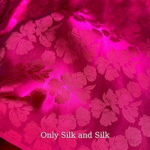 May include: A close-up shot of a bright fuchsia silk fabric featuring a floral design. The fabric has a slight sheen, and the text "Only Silk and Silk" is visible. The floral pattern is a lighter shade of fuchsia.