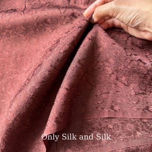Könnte beinhalten: Nahaufnahme eines bordeauxfarbenen Stoffes mit floralem Muster. Der Stoff ist gefaltet und zeigt seine Textur und sein Design. Der Text "Only Silk and Silk" ist unten im Bild zu sehen.